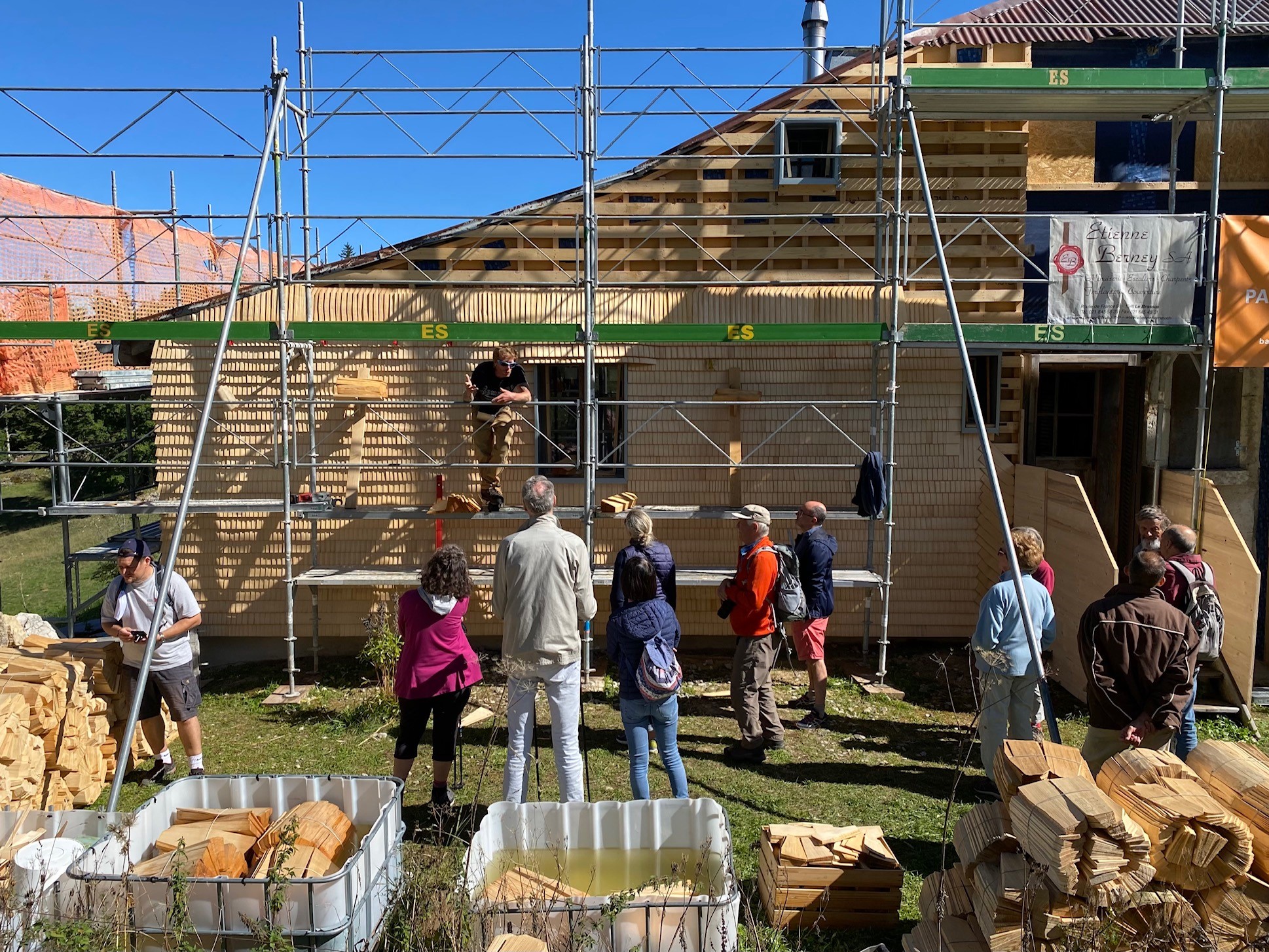 Sur la figure, on peut voir un bâtiment en bois en cours de restauration par plusieurs personnes. 
